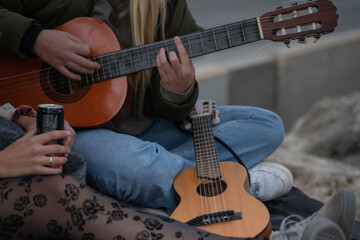 Blonde girl sitting on the rocks by the sea playing guitar and singing in Palma de Mallorca, Spain