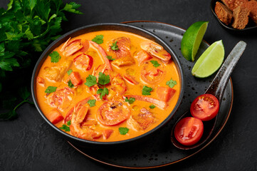Moqueca with Fish and Shrimps in black bowl on dark slate table top. Brazilian sea food curry dish...