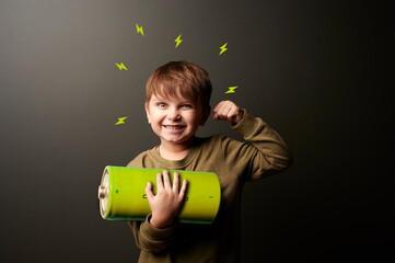 Happy,  boy holding a battery against a black background and demonstrating strength. concept of...