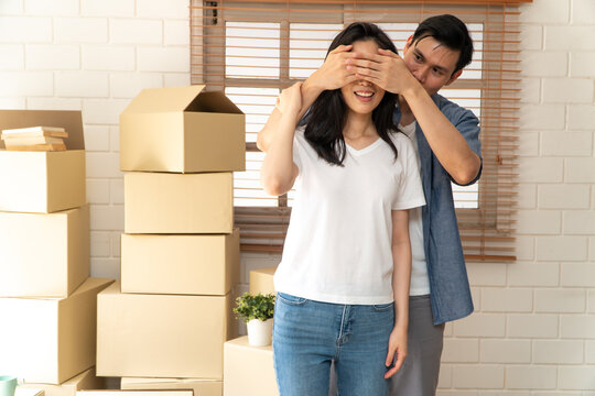 Smiling Young Asian Happy Couple Close Girlfriend Eyes For A Surprise At Moving Day In Their New Home After Buying Real Estate. Concept Of Starting A New Life For A Newly Married Couple.