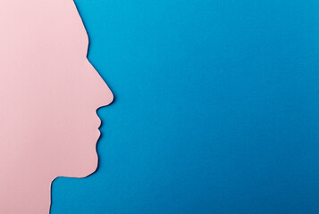 Head silhouette made of paper. Pink paper shaped as a human head with copy space on blue paper background.