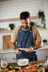 Fototapeta na wymiar Attractive man cooking in modern kitchen. Handsome man playing with flour while preparing delicious food.