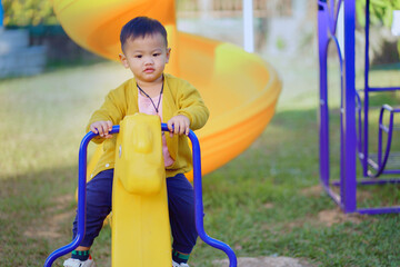 Child playing on the playground, Asian boy aged 1- 2 in Thailand is cute. Younger put on a yellow shirt and sat on a rocking horse in the playground in the morning.