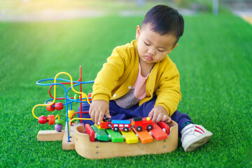 Asian baby boys are playing toys that promote brain and muscular development, A 2-year-old boy in a yellow shirt and blue pants sits on the lawn and casually plays with toys, Child playing.