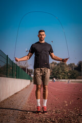 Handsome young man wearing sportswear and jumping with skipping rope during autumn