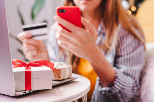 Close up of woman hands with mobile cellphone, credit card, gifts and laptop. Online shopping at Christmas, valentine day or birthday holidays. Freelance girl woking from home office