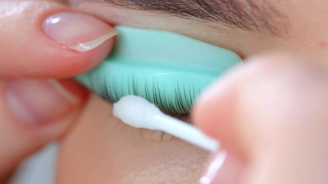Face of a young girl before a modern eyelash lamination procedure in a professional beauty salon. The master applies special glue before the eyelash curling procedure close up.