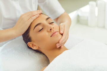 Fototapeta na wymiar Positive relaxed woman getting procedure of facial massage from cosmetologists hands