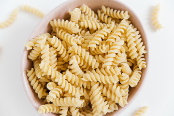 uncooked spiral pasta in the ceramic plate. white background. close-up view.