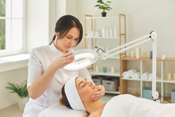 Dermatologist directing lamp to womans face during checking skin