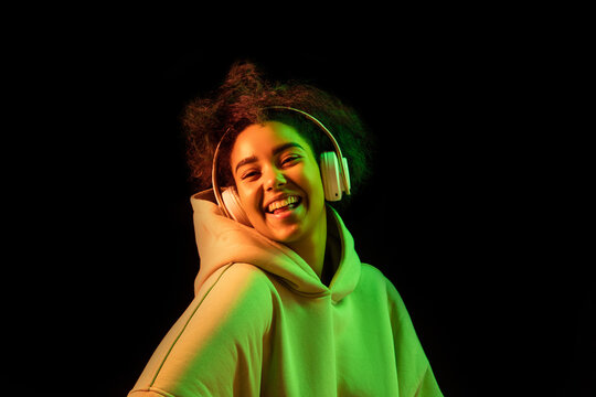 Inspiration. African-american woman's portrait on dark background in orange-green neon. Listening to music with headphones. Concept of human emotions, facial expression, sales, ad, fashion. Copyspace.
