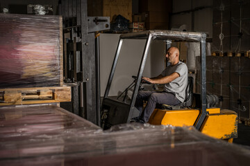 Fototapeta na wymiar Warehouse man worker with forklift. Warehouse worker driver in loading by forklift stack loader