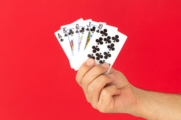 Male hand holding combination of royal flush poker cards on red background. Casino luck fortune...