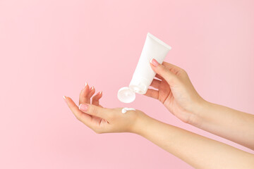 Female hands apply cosmetic skin care moisturizer cream on pink background
