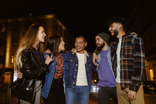 Happy Group Of Friends Walking At Night Out Together In The Streets Of City