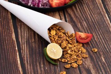Tasty Indian Spicy Traditional Snacks Chatpata Namkeen Chana Jor Garam Masala Roasted Smashed Chickpeas Rolled In White Cone Paper With Mixing Ingredients Spread On Brown Colored Wooden Texture Table