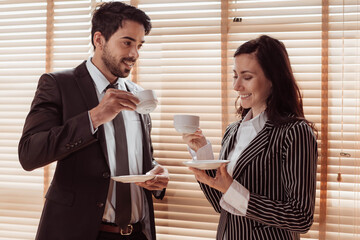 Young business man and woman working together and drinking coffee in office. Two business people drinkking coffee and discuss about project. Business and working concept.