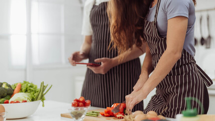Cropped image of romantic couple cutting pepper in kitchen room. Happy couple love cooking together and watching online cookbook in the kitchen.