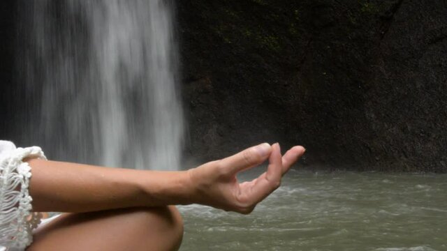 woman doing Yoga and sitting meditation pose at waterfall in the tropics