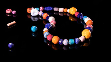 Bright natural multi colored ceramic beads on a black background with reflection. Traditional Slavic culture, hand made jewelry.  