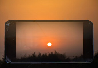 Beautiful orange light of sunrise on screen of mobile phone isolated with background.