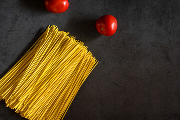 Yellow spaghetti and tomatoes on a black marble table. Yellow Italian Pasta. Raw spaghetti. Italian concept and menu