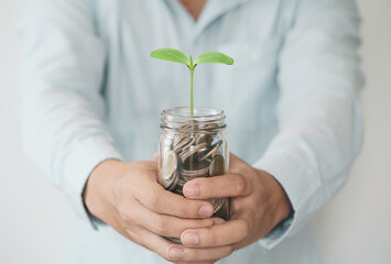 Businessman holding coins in piggy jar with growth plant , investment profit and dividend money...