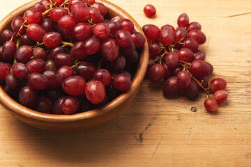 Fresh ripe grape berries in bowl on brown wooden background.