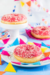 Pink glazed donuts on a light blue background, decorated with streamers and a party garland, focus on the front donut, vertical