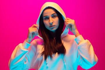 Urban style. Caucasian woman's portrait isolated on pink studio background in mixed neon light. Beautiful female model. Concept of human emotions, facial expression, sales, ad, fashion. Copyspace.