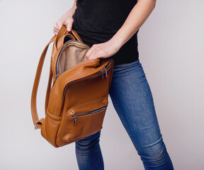 A beautiful, young girl shows a brown, leather backpack in the studio. Leather accessory advertising. Hand luggage. Large, spacious handmade backpack