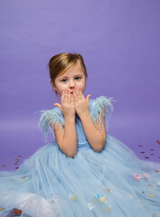 a small beautiful girl in a lush blue dress blows a kiss on a purple background