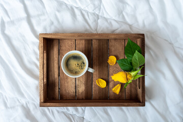 Eine Tasse Kaffee und gelbe Rosen auf einem Holz Serviertabeltt auf einer weißen Bettdecke....