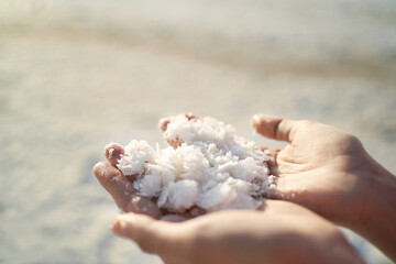Fototapeta na wymiar Close up woman hands holding crystallized salt natural mineral formation at Dead Sea coastline with highlight sunlight at sunset