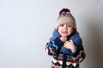 Sick child in clothes, toddler boy is standing on the grey background with a fever. llness child. Boy touches his neck