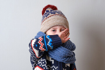 Sick child in clothes, toddler boy is standing on the grey background with a fever. llness child. Boy wipes his nose