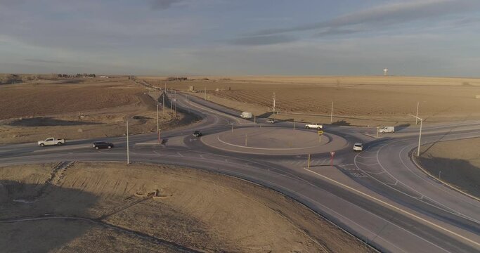 Cars and farm trucks navigate a modern roundabout far from the city.