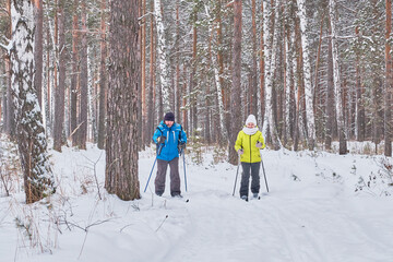 Fototapeta na wymiar Mature couple in winter sportswear are skiing in snowy forest.