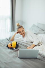 Young woman working on laptop in bed. Young woman in bathrobe working in bed.