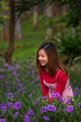 A beautiful Asian woman in a red dress looking at the violet flowers and enjoying her holiday in the garden which is full of purple flowers and green plants.