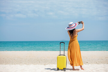 Fototapeta na wymiar Asian women traveler holding yellow luggage walking and take a photo smart phone on the beach. Traveler and Tourism planning trips summer vacations with Traveler summertime.