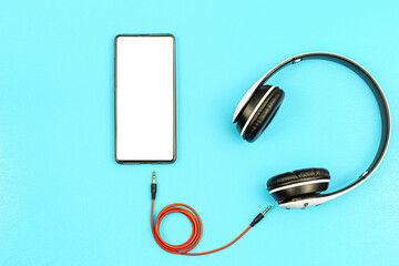 Top view of white headphones and black cell phone on blue background with copy space. Flat lay.