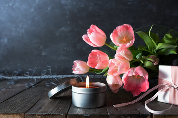 Atmospheric mothers day decoration with bouquet of pink tulips and gift on dark vintage wood. Space for text.