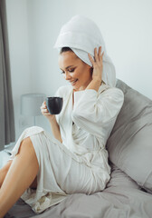 Young woman in bathrobe drinking coffee in bedroom.