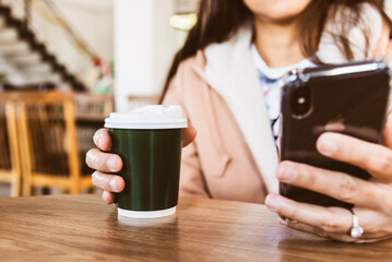 Woman holding coffee to go cup and looking at smartphone while sitting and chilling.