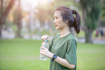 Young Asian woman drinking water after work out in the park