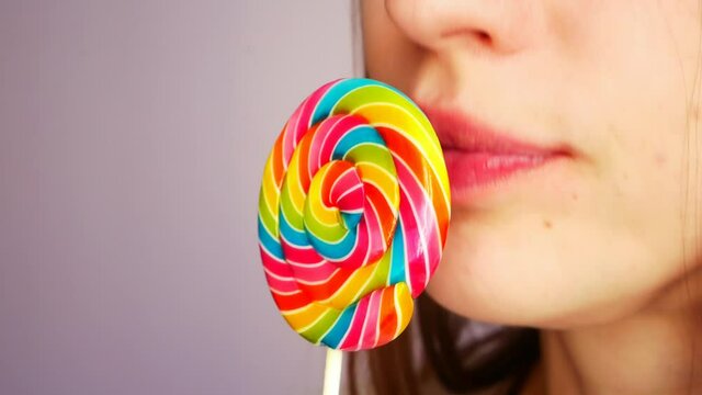 Close-up of a lower part of the face of young lady licking a beautiful multicolored lollipop