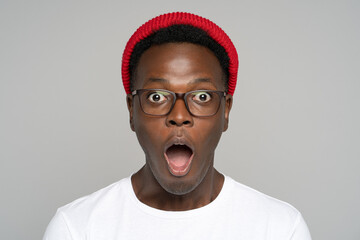 Surprised afro young man makes big eyes opens mouth widely, shocked with unprecedentedly low...