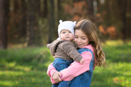 Young Girl Hold  Little Baby Brother In Spring Nature. Family And Siblings Love Concept. 