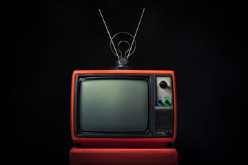 Retro old red TV with antenna on wooden box on black background.